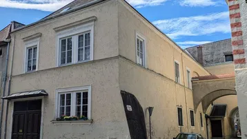 Historisches Gebäude mit Putzfassade, Sprossenfenstern und einem Durchgangsbogen zur Straße.