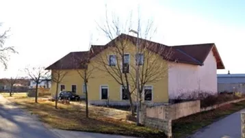 Gelbes Gebäude mit rotem Ziegeldach und kahlen Bäumen an einer Straße im Winter.