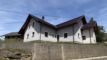Ländliches Einfamilienhaus mit Satteldach und grauer Fassade, umgeben von grüner Natur.