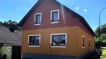 Zweistöckiges Einfamilienhaus mit rot-orangefarbener Fassade und Satteldach unter blauem Himmel.