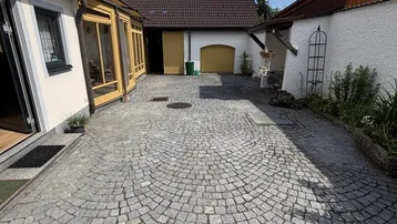 Gepflasterter Innenhof mit Zugang zu verschiedenen Gebäudeteilen unter blauem Himmel.