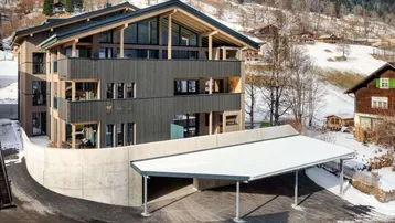 Modernes Gebäude mit Holzfassade und Carport in verschneiter Berglandschaft.