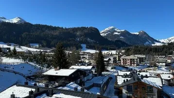 Panoramablick auf eine verschneite Berglandschaft mit traditionellen Häusern unter blauem Himmel.