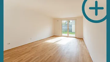 Helles, leeres Zimmer mit Parkettboden und Zugang zu einem kleinen Gartenbereich.