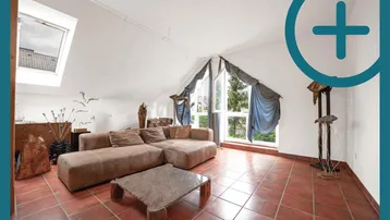 Gemütliches Wohnzimmer im Dachgeschoss mit Schrägfenstern, bequemer Couch und Terrakottafliesen.