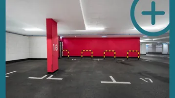 Tiefgarage mit markierten Parkplätzen, roter Wand und Absperrungen für einzelne Stellplätze.