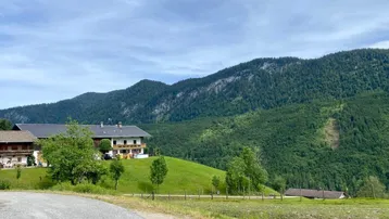 Weitläufige Landschaft mit grünen Hügeln und bewaldeten Bergen unter bewölktem Himmel.