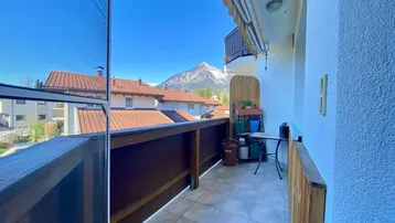Sonniger Balkon mit Fliesenboden, Holzbalkonbrüstung und Bergblick in die Ferne.