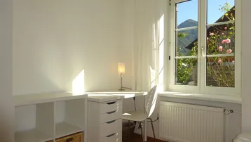 Freundliches Schlafzimmer mit Arbeitsbereich, Holzfußboden und Fensterblick auf die Berge.