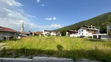 Weitläufiges Grundstück mit Blick auf die umliegende Berglandschaft und Dorfkirche.
