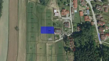 Luftaufnahme eines Wohngebiets mit Feldern und Parzellen, wobei ein Grundstück blau markiert ist.