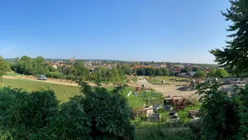 Panoramablick über eine ländliche Landschaft mit einem Dorf in der Ferne und einer Baustelle im Vordergrund unter blauem Himmel.