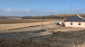 Einfamilienhaus in ländlicher Umgebung mit weitem Blick über Felder und Windräder unter blauem Himmel.