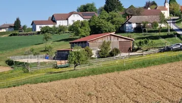 Ländliche Szenerie mit mehreren Häusern auf einem Hügel, Feldern und einem landwirtschaftlichen Gebäude.
