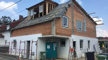 Haus im Bauzustand mit sichtbarer Ziegelmauer und Dachkonstruktion, bereit für weitere Arbeiten.