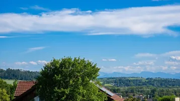 Panoramablick auf ferne Berge über einer grünen Hügellandschaft mit verstreuten Häusern.