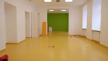 Geräumiger Innenraum mit gelbem Linoleumboden, weißen Wänden und einer grünen Akzentwand, ideal für Kinderaktivitäten.