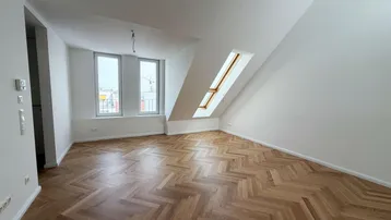 Helles Dachgeschosszimmer mit Fischgrätparkett und Dachfenstern, ideal als Wohn- oder Schlafbereich.