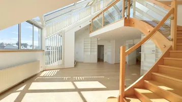 Helles, offenes Wohnzimmer mit Holzparkett, Dachfenstern und einer eleganten Holztreppe zur Galerie.