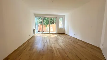 Helles Wohnzimmer mit Holzboden und Zugang zu einer Terrasse oder Gartenbereich.