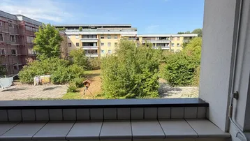 Balkon mit Markise und Blick auf die grüne Umgebung und umliegende Gebäude.