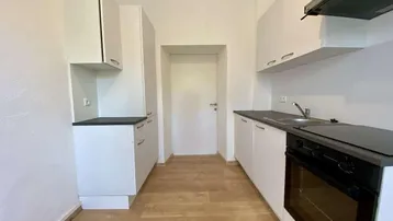 Moderne Küche mit weißen Schränken, dunkler Arbeitsplatte und integriertem Backofen.