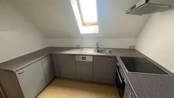 Kompakte Küche im Dachgeschoss mit grauen Schränken, Einbaugeräten und Dachfenster.