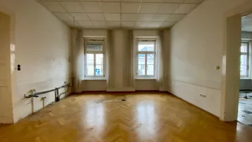 Geräumiger Innenraum mit Fischgrätparkett und zwei Fenstern, bereit für Renovierung und individuelle Gestaltung.