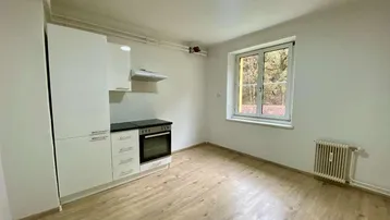 Heller Raum mit integrierter Küchenzeile, Fenster und Laminatboden.