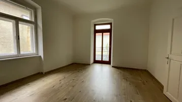 Heller Raum mit neuem Holzparkettboden und Zugang zu einem französischen Balkon.