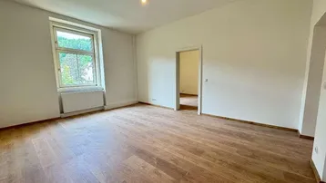 Heller, leerer Raum mit Holzfußboden und großem Fenster, bereit zur individuellen Gestaltung.