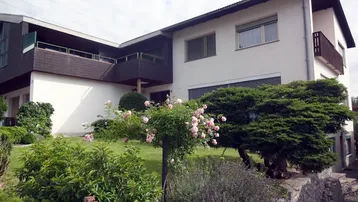 Mehrfamilienhaus mit gepflegtem Vorgarten, blühenden Rosen und Balkonen.