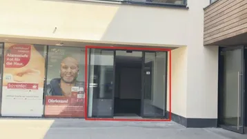 Moderne Ladenfront eines Geschäftsraums mit großer Glasfassade und Werbeplakaten im Erdgeschoss.