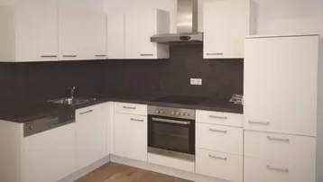 Moderne Einbauküche mit weißen Schränken, dunkler Arbeitsplatte und Edelstahlgeräten.