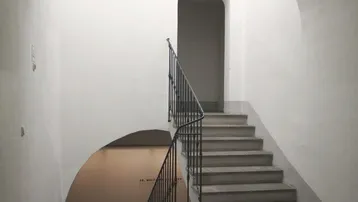 Heller Treppenaufgang mit gewölbter Decke und schmiedeeisernem Geländer in einem historischen Gebäude.