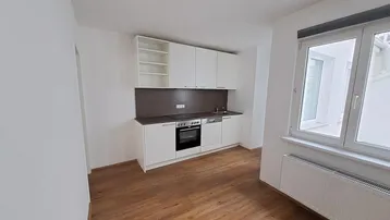 Helle Küchenzeile mit weißen Schränken, integriertem Backofen und Laminatboden.