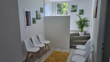 Heller Wartebereich mit modernen weißen Stühlen, Laminatboden und einer Treppe, die in den oberen Bereich führt.