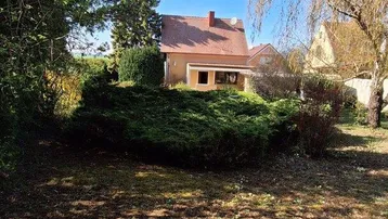 Blick auf das Haus von der großen, grünen Gartenfläche mit Bäumen und Sträuchern.