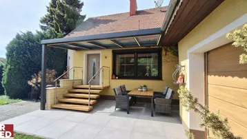 Überdachte Terrasse mit Sitzgelegenheiten und Zugang zum Haus, ideal für entspannte Stunden im Freien.