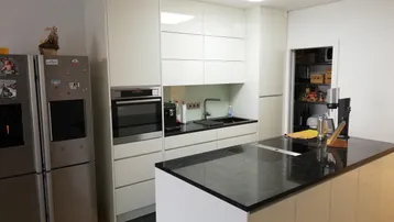 Moderne Küche mit weißen Hochglanzfronten, schwarzer Arbeitsplatte und integrierten Geräten sowie einer Speisekammer.