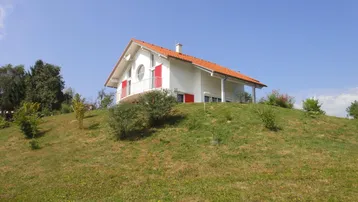 Freistehendes Haus mit weißer Fassade und rotem Ziegeldach auf einem sonnigen Hügelgrundstück mit Weitblick.