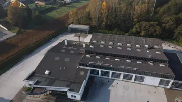 Luftaufnahme eines Gewerbegebäudes mit großem Parkplatz und angrenzendem Wohngebiet in ländlicher Umgebung.
