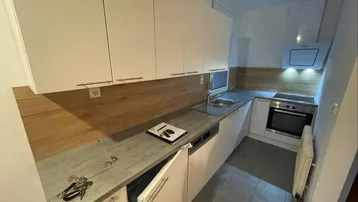 Moderne Einbauküche mit weißen Schränken, Holzrückwand und integrierten Geräten.