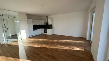 Helles, offenes Wohnzimmer mit integrierter Küche, Holzboden und Zugang zum Balkon.