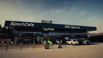 Modernes Geschäftsgebäude mit großen Glasfronten, das ein Sportcafé und Fitnessstudio beherbergt.