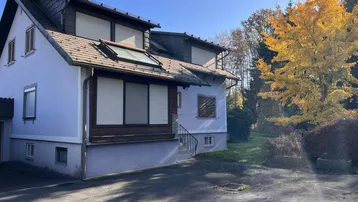 Vorderansicht des Hauses mit Dachfenstern, Rollläden und einer gepflasterten Auffahrt.