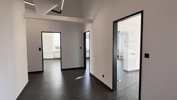 Heller Flur mit dunklen Fliesen und modernen Glastüren, der zu verschiedenen Büroräumen führt.