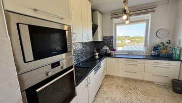 Moderne Küche mit weißen Schränken, schwarzer Arbeitsplatte, integrierten Geräten und weitem Ausblick.