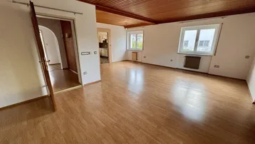 Geräumiges Wohnzimmer mit hellem Laminatboden und Holzdeckenverkleidung, bietet viel natürliches Licht.