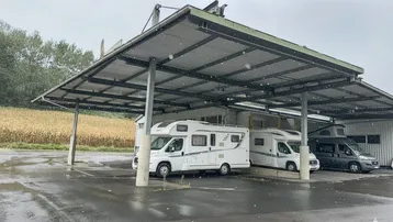 Überdachter Stellplatz für Wohnmobile mit Solaranlage auf dem Dach und Blick auf die umliegende Landschaft.